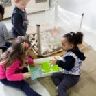 Quatro crianças brincam sentadas em sala de aula