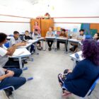 Alunos em sala de aula, sentados em roda, ouvem