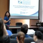 Servidora segura microfone e olha para plateia durante apresentação de projeto