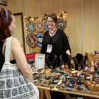 Expositora de acessórios sorri para mulher que olha seus produtos