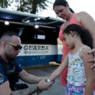 Guarda Municipal coloca fita de identificação em braço de menina, ao lado da mãe