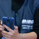 Imagem de uma recenseadora, com colete do IBGE, manuseando celular