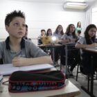 Alunos em carteiras e cadeiras em sala de aula olham para frente