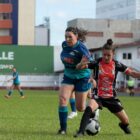 Duas jogadoras de futebol disputam bola em campo
