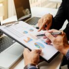 Dois homens apontam para planilha, com notebooks a frente