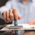 Homem segura carimbo em direção a papéis em uma mesa