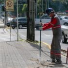 Homem, com capacete e uniforme, trabalha com ferramenta em frente ao prédio verde