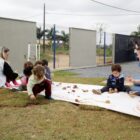 Duas professoras e alunos sentados em tecido em gramado em centro de educação infantil