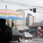 Pessoa segura guarda-chuva e caminha por rua durante chuva