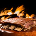 Imagem de um prato de costela bovina assada com fogo atrás