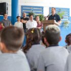 Prefeito discursa em escola e alunos uniformizados e sentados, prestam atenção