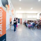 Mulher segura microfone e fala para plateia sentada