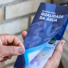 Mão de mulher segura folheto com relatório da Companhia Águas de Joinville