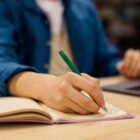 Detalhe de mão de pessoa segurando lápis e escrevendo em caderno