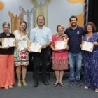 Pessoas abraçadas, com certificado nas mãos, posam para foto