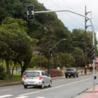 Imagem de um novo semáforo implantado em rua, carros passam, tem árvores ao lado