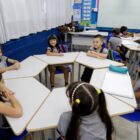Alunos sentados em cadeira na frente de mesas em formato de trapézio