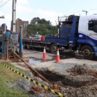 Homens em máquina trabalham em área para instalar tubulação, caminhão estacionado ao lado