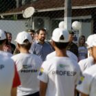 Alunos uniformizados e com boné observam secretário de educação em evento