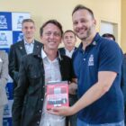 Prefeito abraça autor segurando livro, observado por outras autoridades