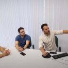 Três homens sentados olham para monitor