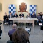 Prefeito fala em microfone ao lado de autoridades em coletiva de imprensa