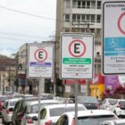 Foto de rua com carros estacionados e placas do estacionamento rotativo