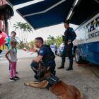 Guardas municipais com cachorro interagem com pessoas perto de base
