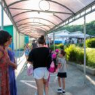 Entrada de uma escola com mãe entrando com a filha e professora as recebendo