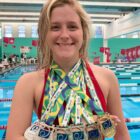 Atleta de natação posa para foto com medalhas penduradas no pescoço