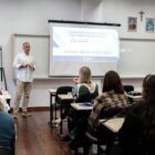 Palestrante em frente de uma sala fala para pessoas sentadas em cadeiras