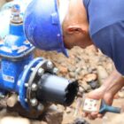 Trabalhador com uniforme e capacete segura equipamento perto de tubulação