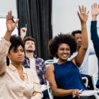 Pessoas com mãos levantadas olham para frente e participam de encontro
