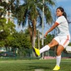 Garota com uniforma chuta bola em campo de futebol