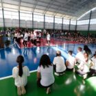 Estudantes sentados observam apresentação de dança de outros alunos, na frente de autoridades, durante inauguração da quadra