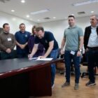 Prefeito assina documento em seu gabinete, observado por autoridades