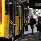 Ônibus de transporte coletivo parado em terminal e passageiro embarca enquanto outra mulher caminha ao lado do ônibus