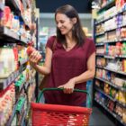 mulher em corredor de supermercado segura cesta de compras e olha e segura produto em outra mão