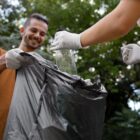 Homem com luvas segura saco de lixo enquanto mulher com luvas deposita conteúdo
