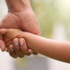 Mão de adulto segura a mão de uma criança