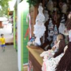 Casinha com produtos artesanais como bonecas de pano em praça onde pessoas passeiam