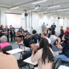 Plateia sentada olha para grupo se apresentando em abertura de conferência