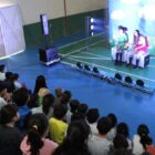 Duas atrizes em palco se apresentam para plateia com alunos