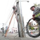 Trabalhador com uniforme e capacete enrola fios sem uso em rua perto de poste