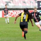 Duas jogadoras de futebol disputam bola em campo