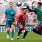 Goleiro se adianta para agarrar bola, em frente a três jogadores
