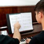 Professor ensina partitura a aluno na frente de um piano