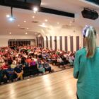 Prefeito e primeira dama em palco falam para plateia sentada