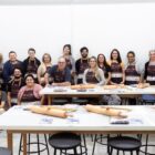 Alunos com avental posam para foto em frente a mesas