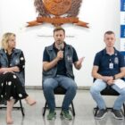 Autoridades sentadas olham para plateia, prefeito segura microfone